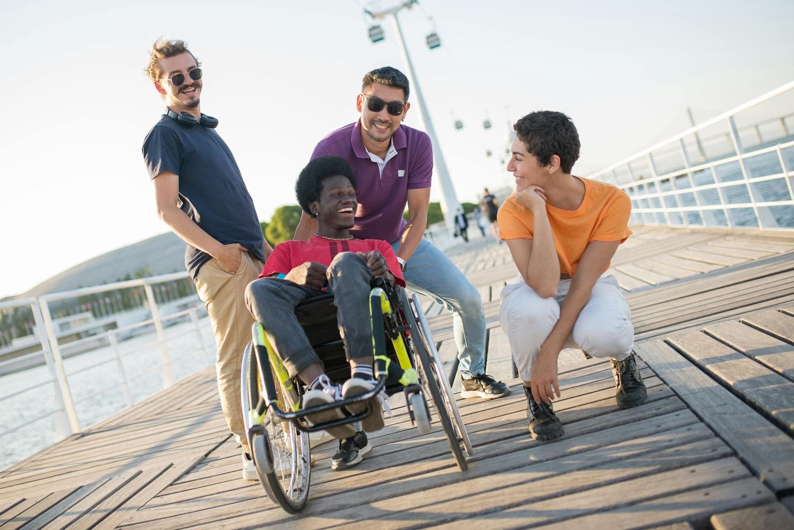 A group of friends laughing together outdoors, including a young person who uses a wheelchair